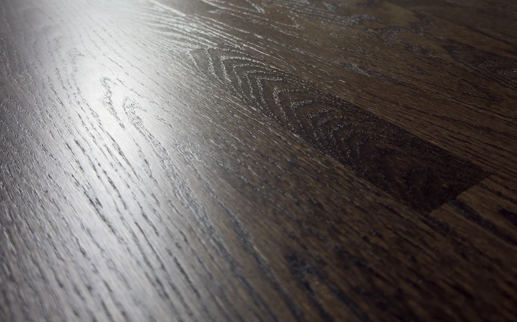 Close-up of refinished dark oak, the grain running unbroken across the board seams under an even sheen